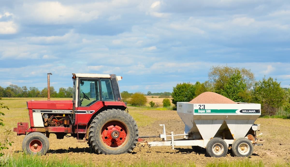 Tractor pulling a loaded broadcast fertilizer spreader hopper in a field