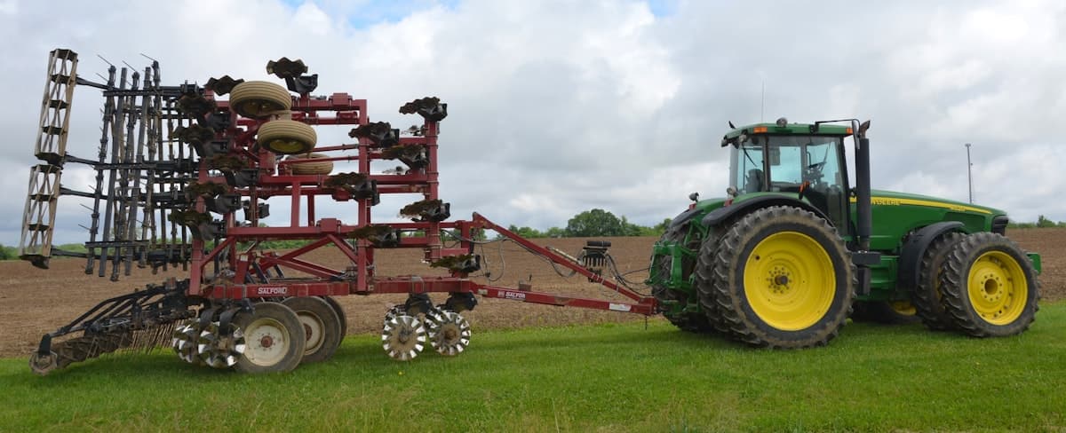 Red trailed field cultivator with rolling harrow hitched to a green tractor
