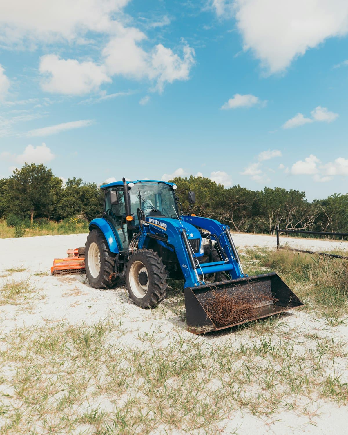 Blue compact utility tractor with front loader bucket parked on a farm