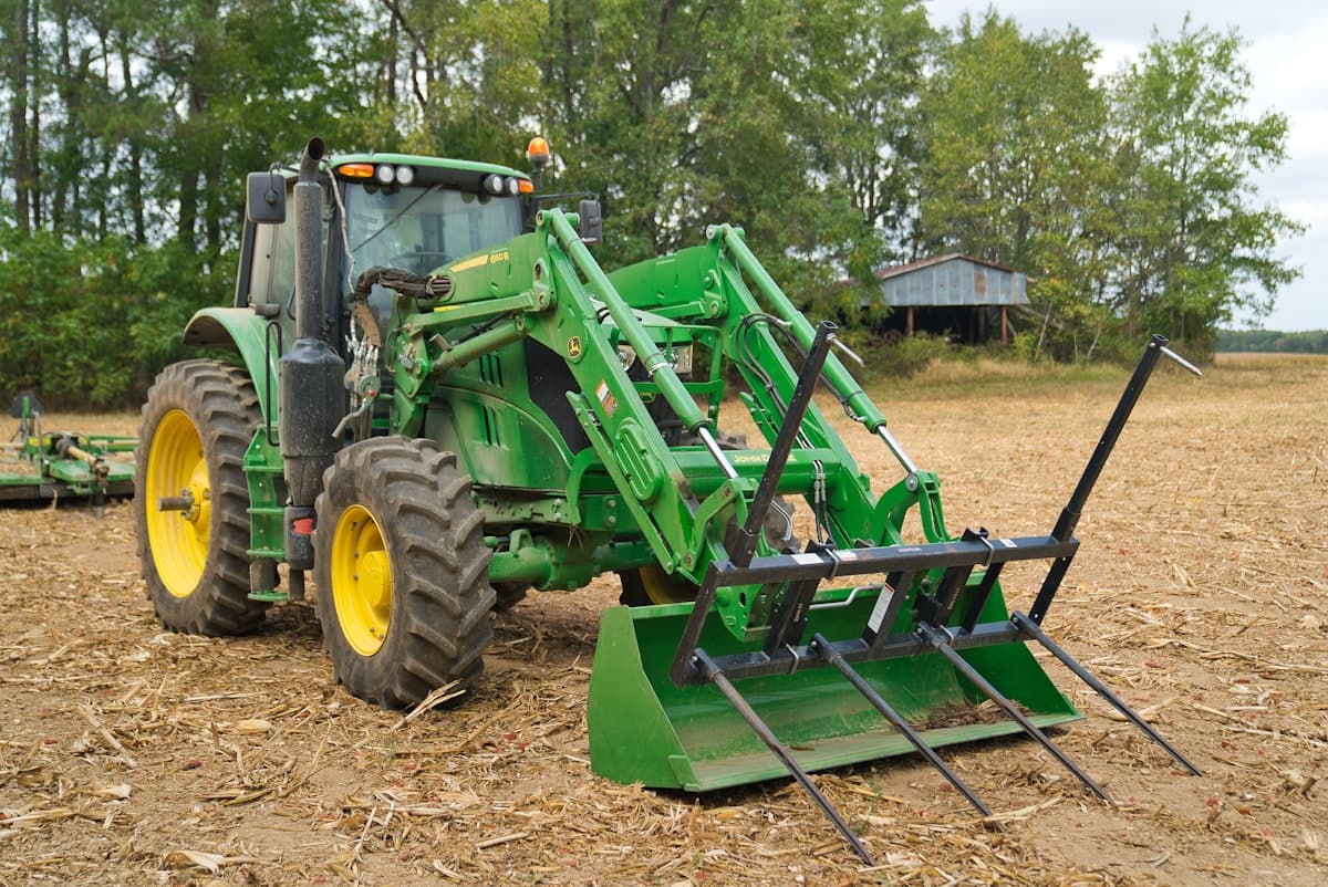 Green heavy-duty farm tractor with front loader and bale spear attachment