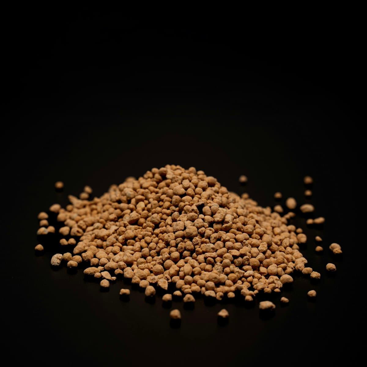 Pile of golden-brown pelletized poultry litter granules on a dark background